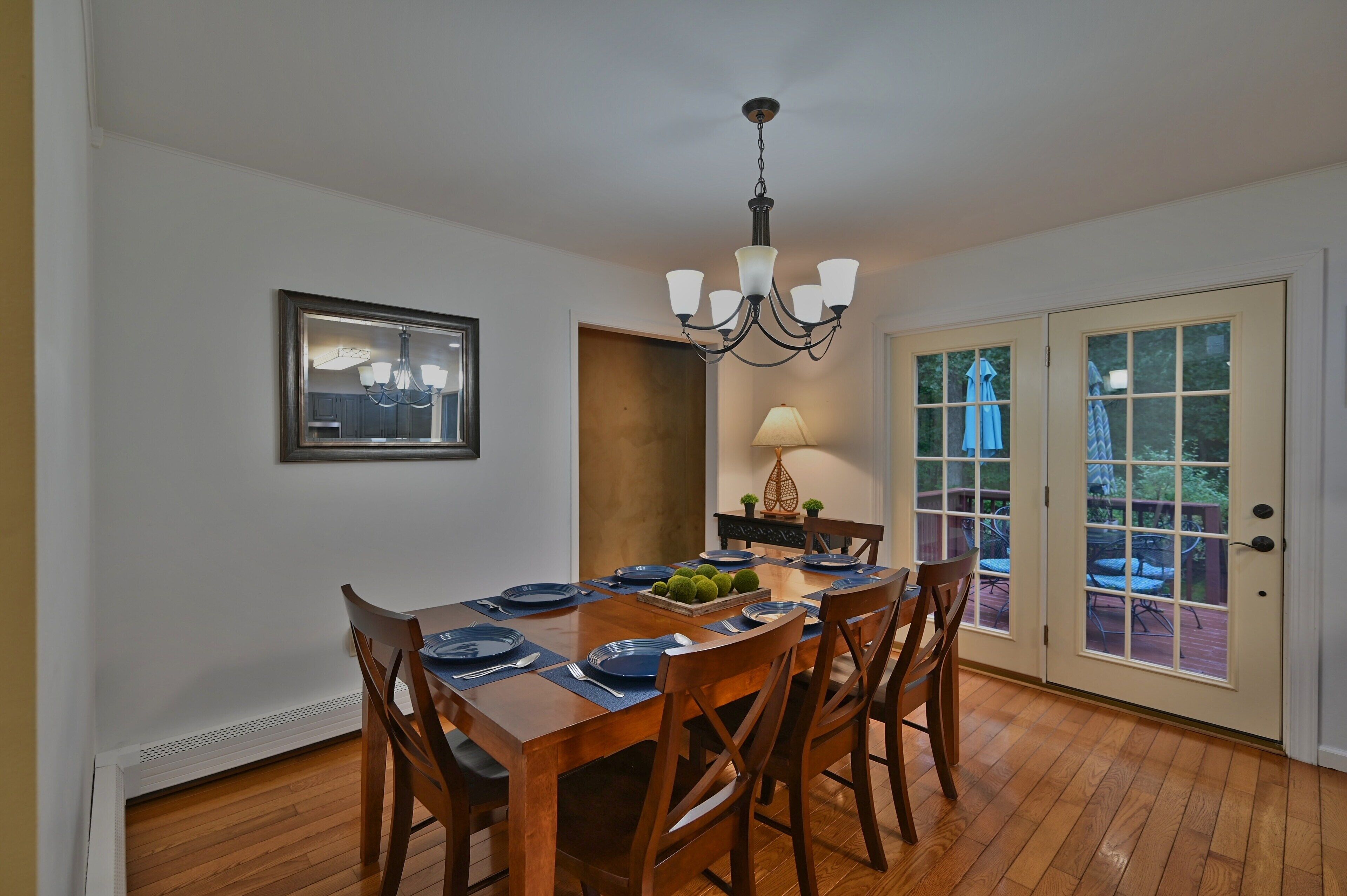 A dining area with a wooden table set for six, a chandelier, and a door leading to an outdoor patio.