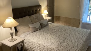 A bedroom with a large bed, two bedside tables with lamps, a door, and a window with curtains. - Gite Campanula with communal swimming pool (Saint-Rémy-de-Provence)