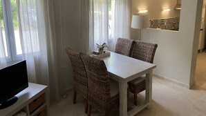 A dining area with a white table and wicker chairs, a TV on a stand, and sheer curtains. - Gite Campanula with communal swimming pool (Saint-Rémy-de-Provence)