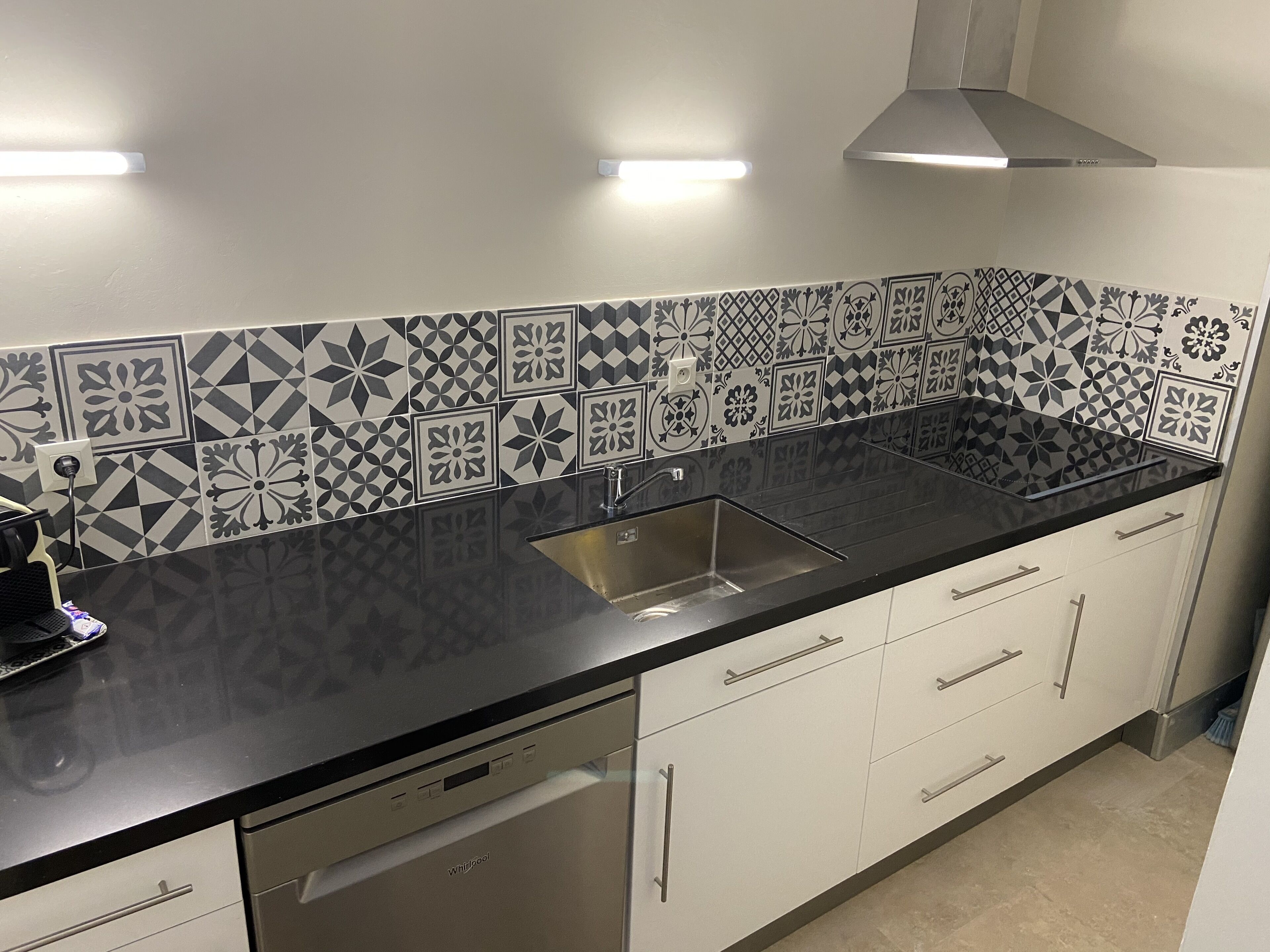 A kitchen with a black countertop, white cabinets, and patterned backsplash tiles.