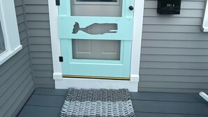 Una puerta azul claro con una ventana, un buzón y un felpudo sobre un porche gris.
