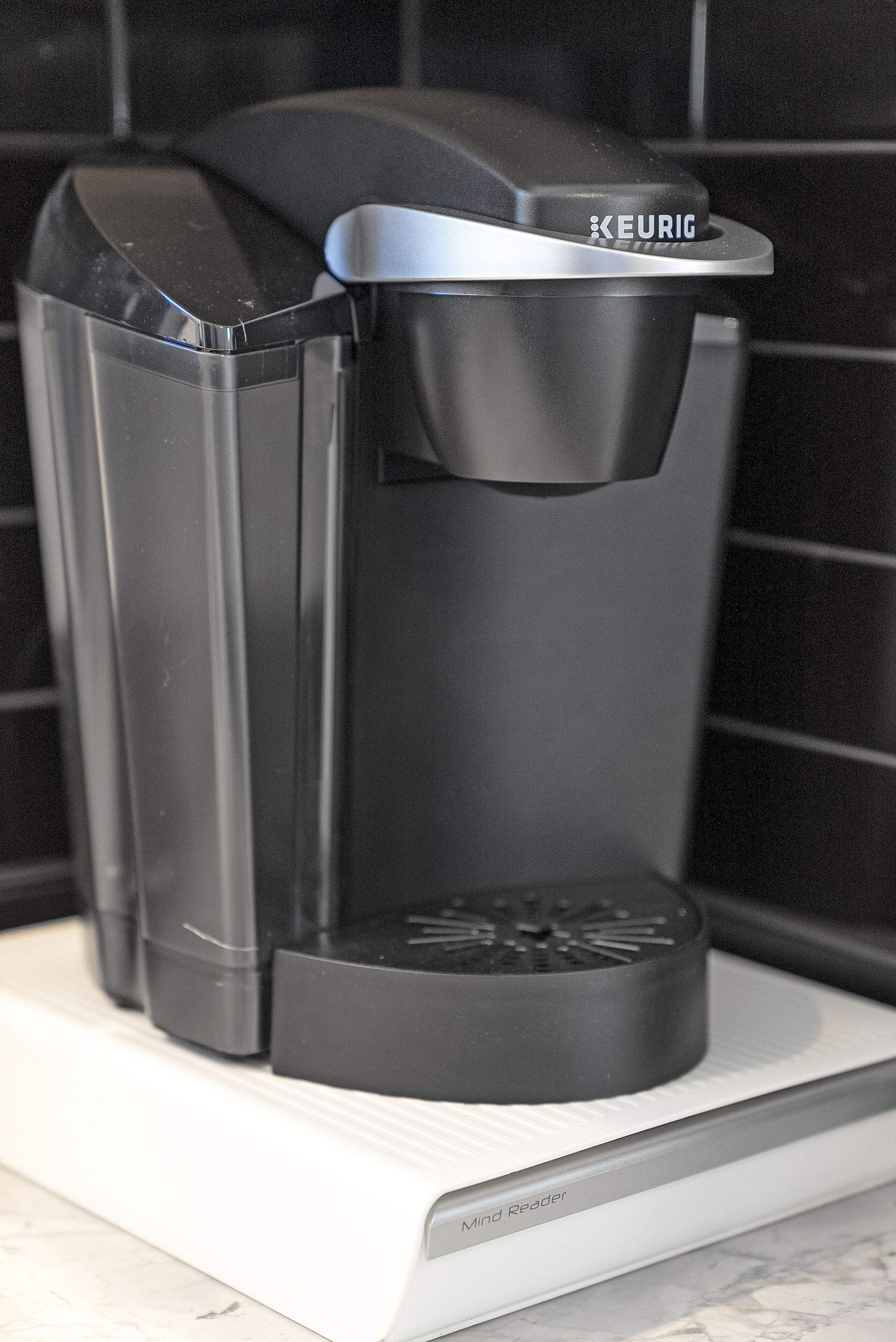 Une machine à café Keurig noire, posée sur un comptoir blanc.