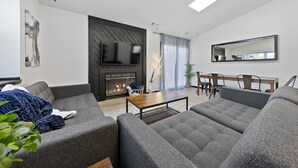 Una sala de estar moderna con chimenea, sofás grises, una mesa de centro de madera y un comedor con sillas y una mesa.