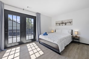 A bedroom with a large bed, two bedside lamps, a ceiling fan, and a window with a view of a wooden deck.