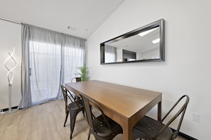 A dining area with a wooden table, four chairs, a large mirror, and a floor lamp.