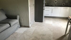 A living room with a grey sofa, a kitchen with white cabinets, and a tiled floor. - Gite Gardenia with a communal swimming pool (Saint-Rémy-de-Provence)