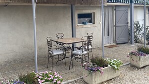 An outdoor patio with a table and chairs, a thatched roof, and flower planters. - Gite Gardenia with a communal swimming pool (Saint-Rémy-de-Provence)