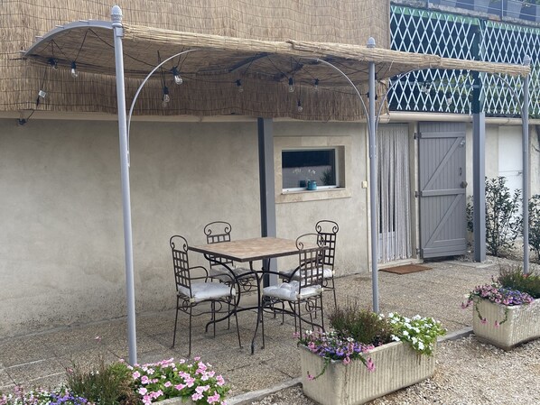 An outdoor patio with a table and chairs, a thatched roof, and flower planters.