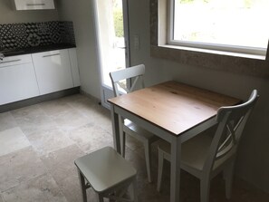 A small kitchen with white cabinets, a wooden table, and two white chairs.