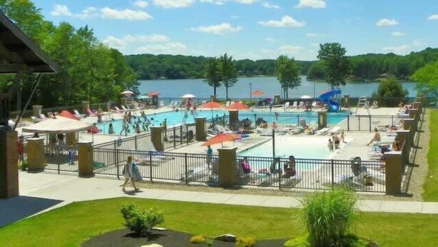 Ein Poolbereich mit mehreren Pools, Sonnenschirmen und Blick auf einen See.