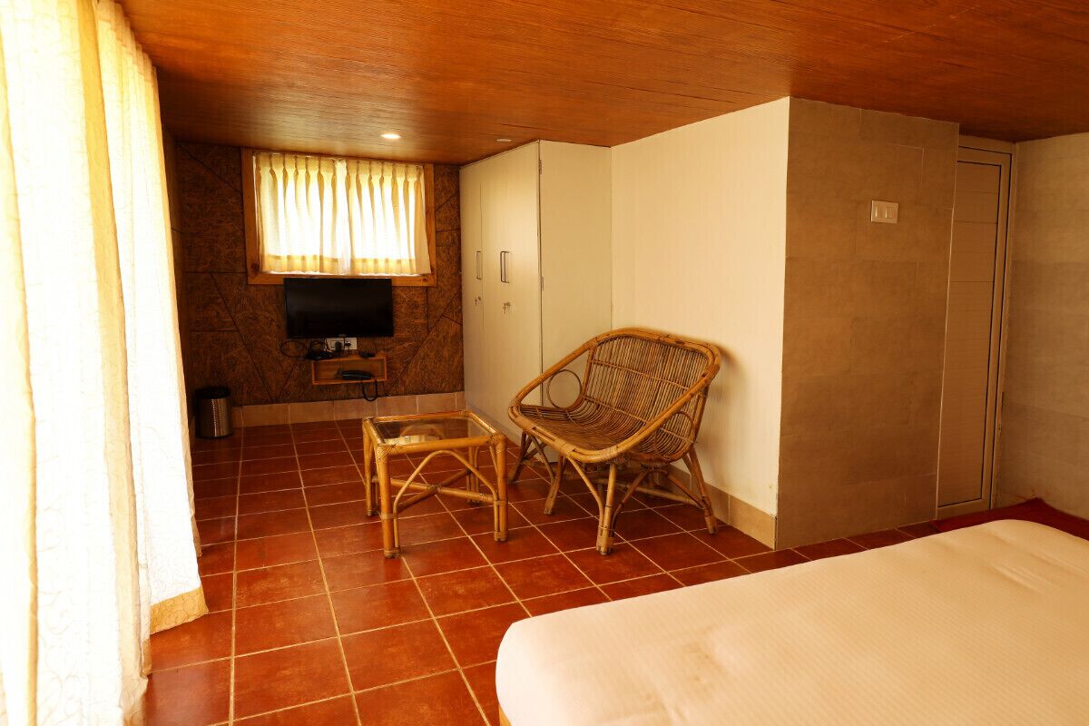 Une chambre d’hôtel comprenant un lit, une télévision, un fauteuil en osier, une petite table et une armoire.