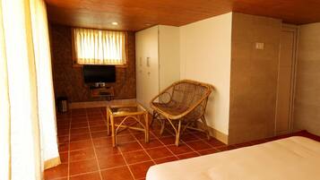 Une chambre d’hôtel comprenant un lit, une télévision, un fauteuil en osier, une petite table et une armoire.