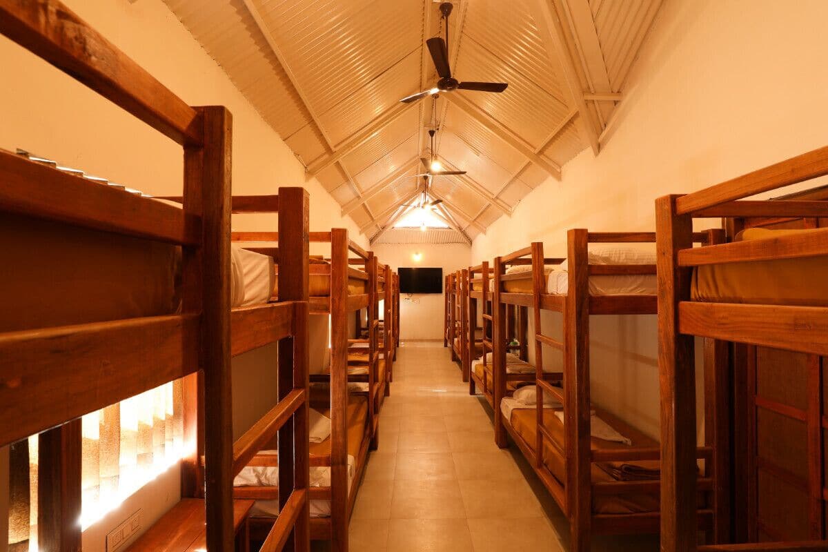 Un couloir bordé de lits superposés de part et d’autre, avec un ventilateur de plafond et un luminaire.