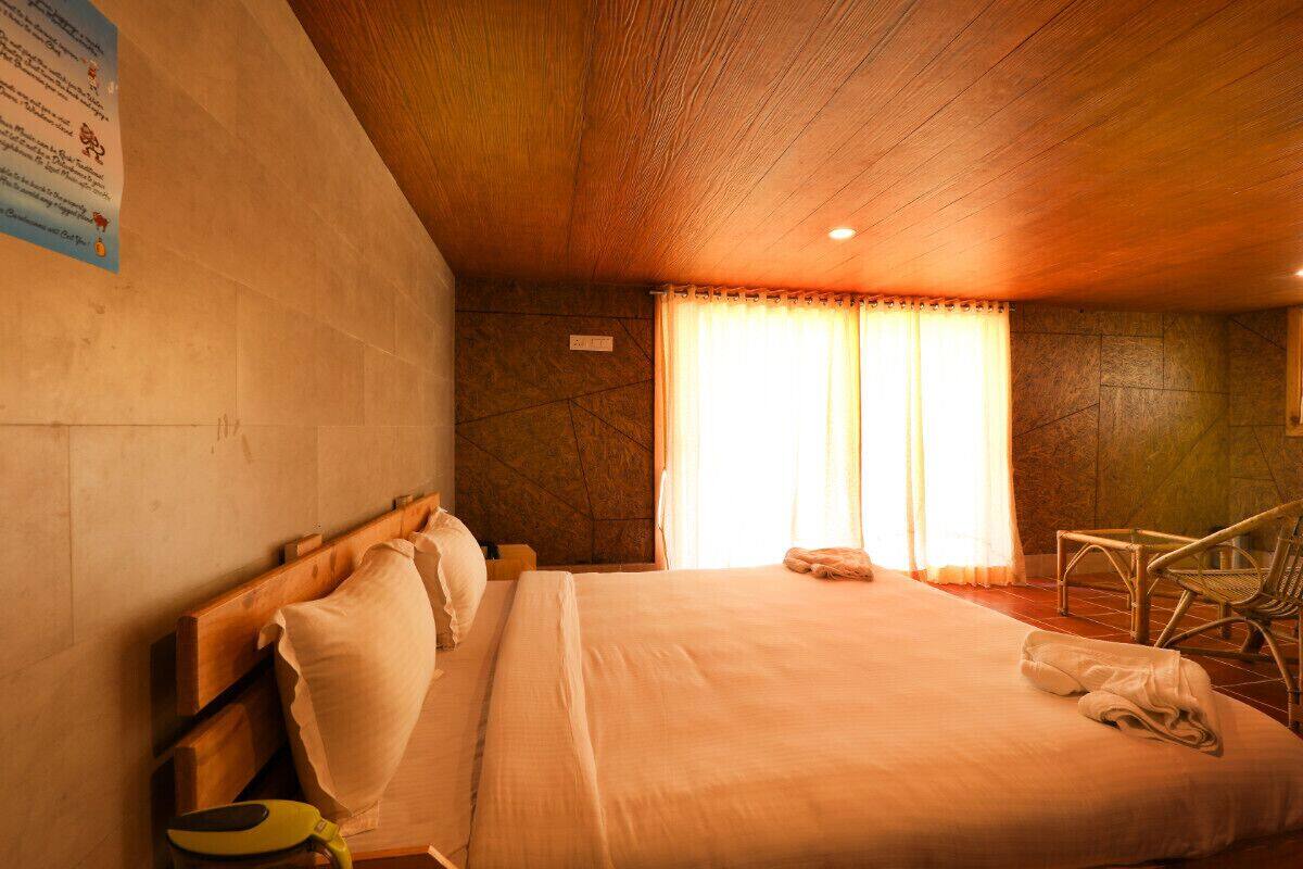 Une chambre d’hôtel avec un plafond en bois, un lit avec du linge de lit blanc, une chaise et une fenêtre avec des rideaux.