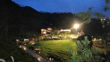 A well-lit resort area with a grassy lawn, pathways, and a building with multiple levels and balconies.