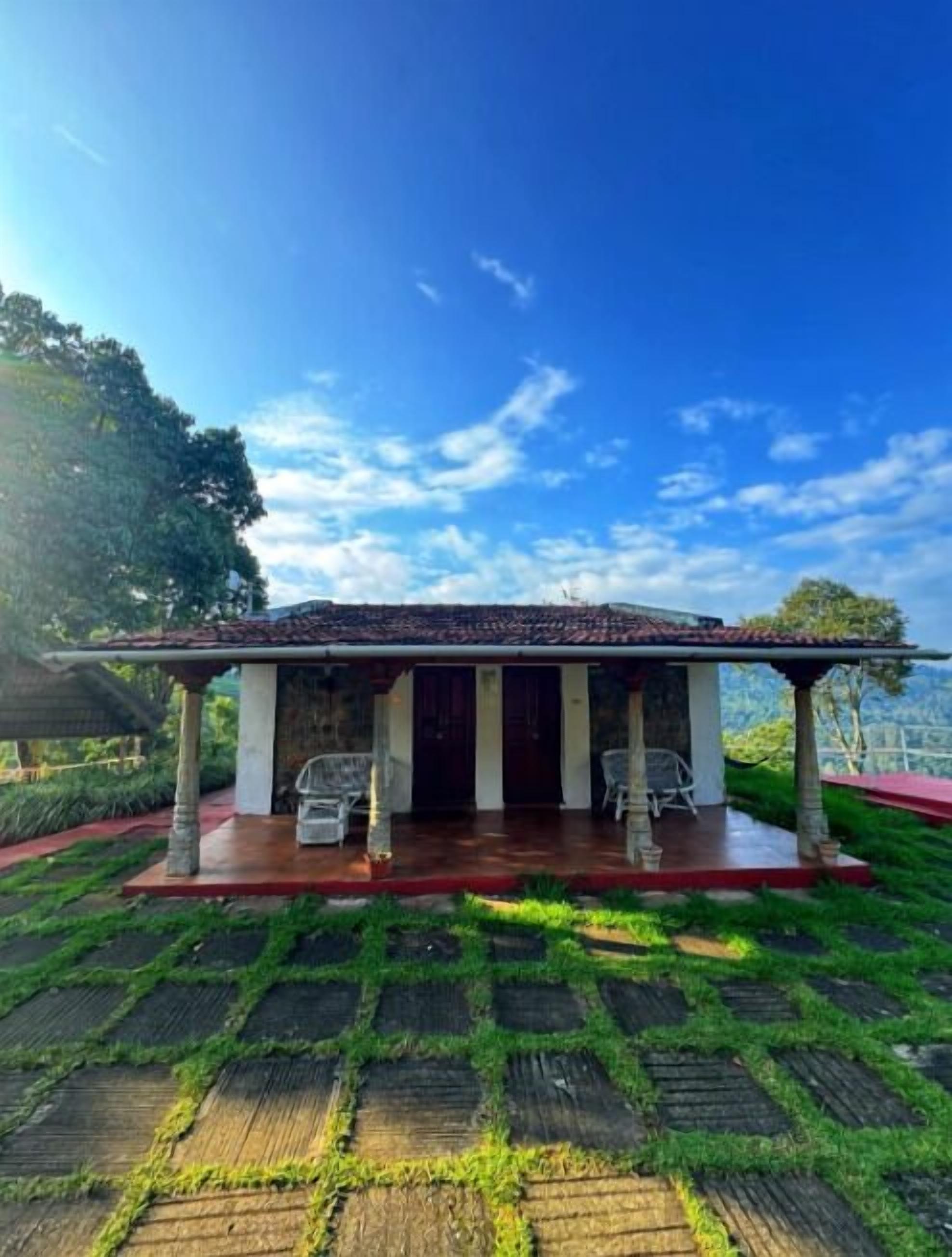 A house with a covered porch, two chairs, and a view of a green landscape.