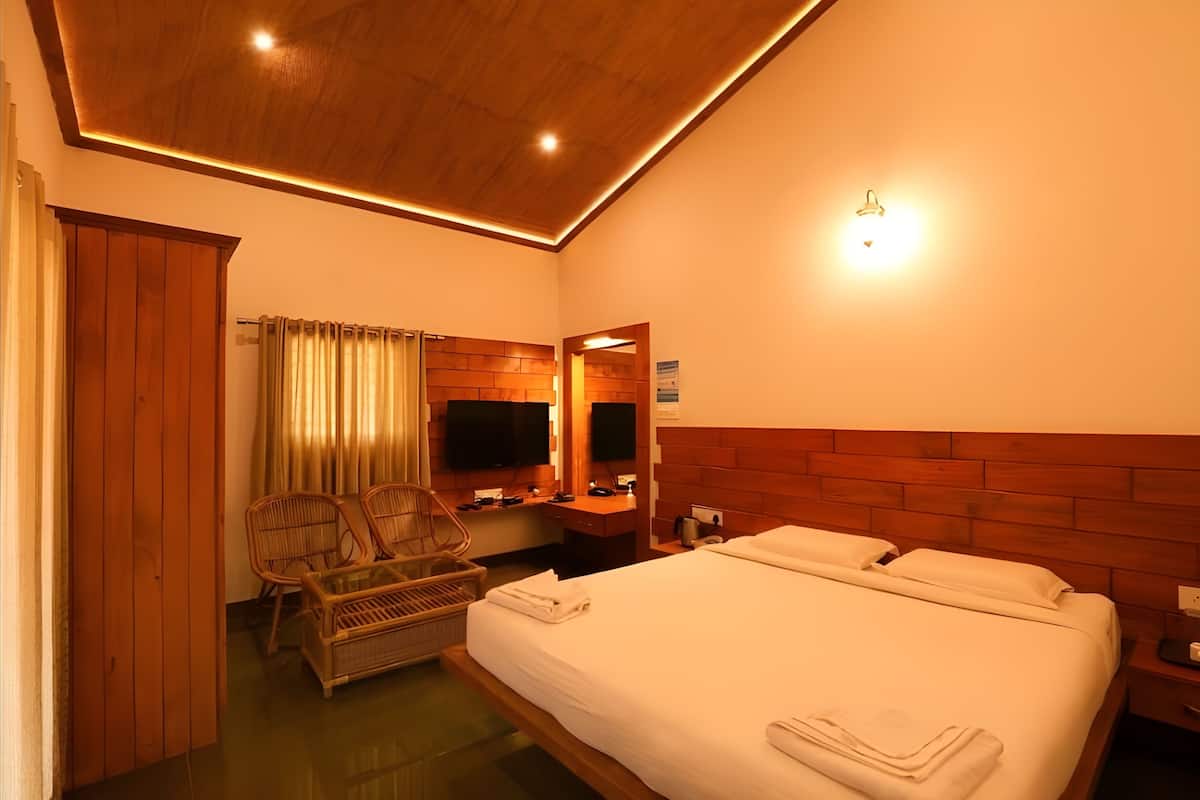 Une chambre d’hôtel avec un plafond en bois, un lit avec du linge de maison blanc, une tête de lit en bois, une télévision, un bureau avec une chaise et une fenêtre avec des rideaux.