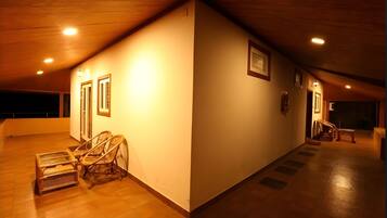 A spacious, well-lit interior with wooden flooring, a high ceiling, and a long corridor with doors and framed pictures.