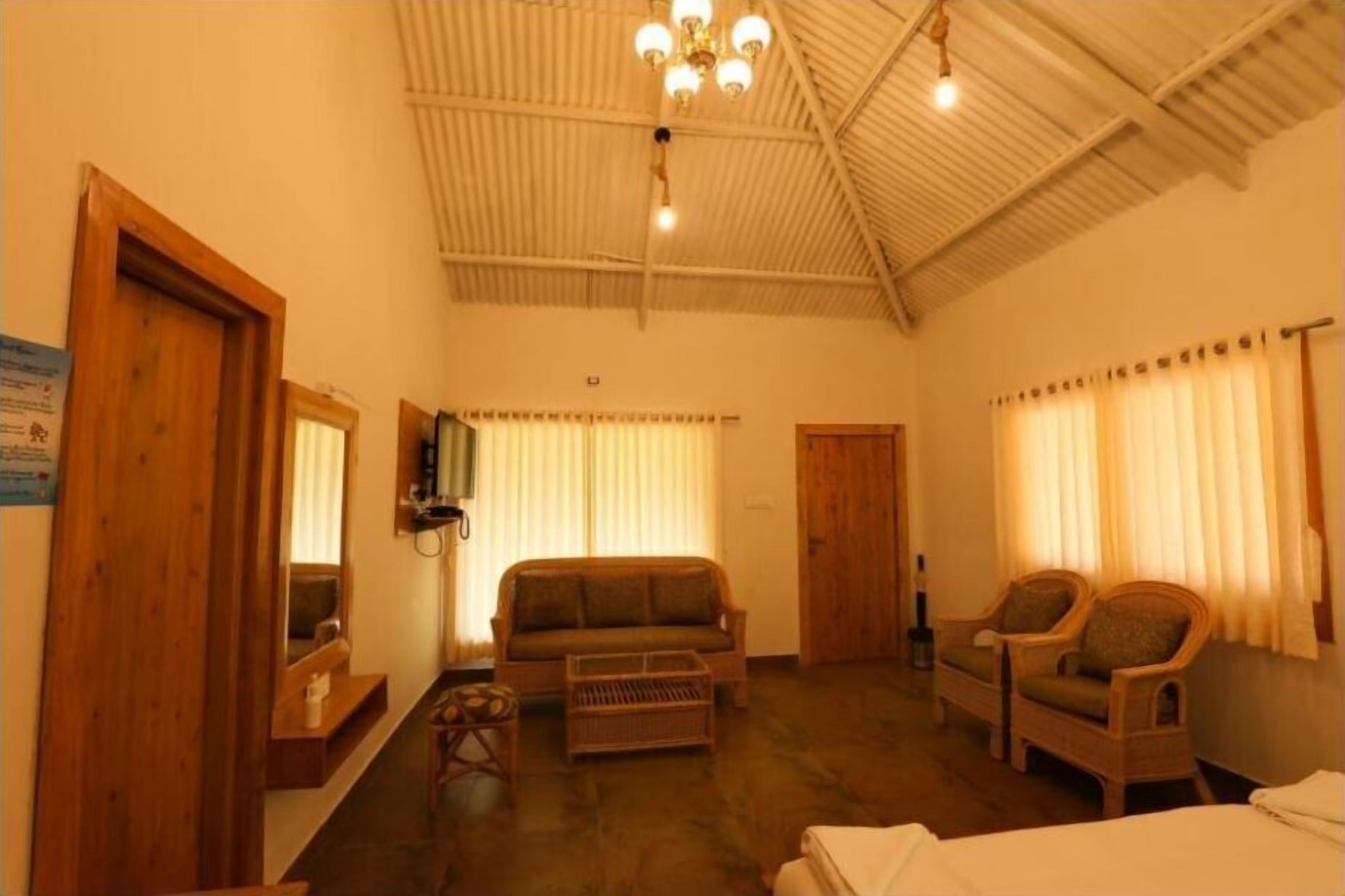 A room with a high ceiling, a sofa, two armchairs, a small table, and a bed.