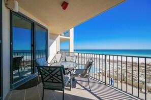 Un balcon avec une table et des chaises, donnant sur une plage sous un ciel bleu azur.