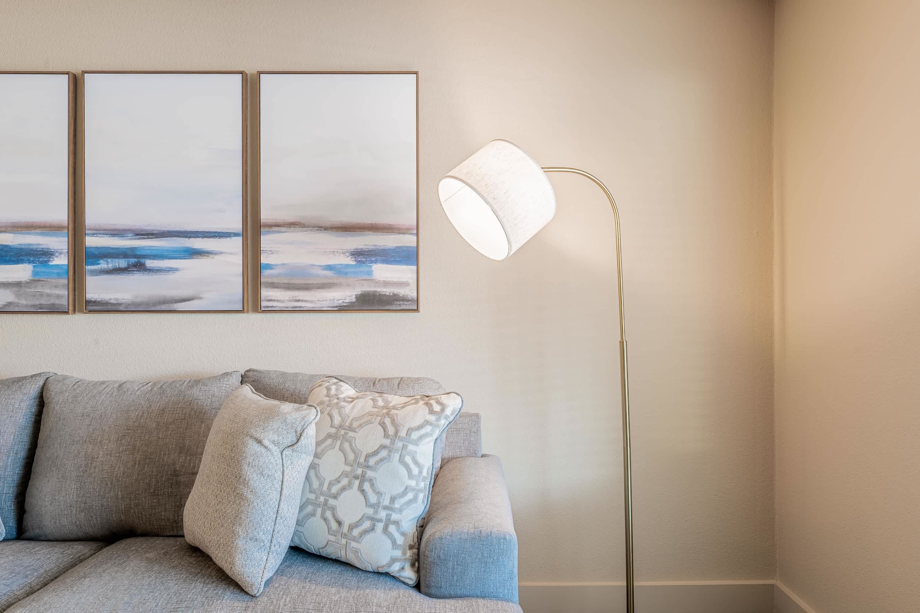 A modern living room with a grey sofa, patterned cushions, and a floor lamp.
