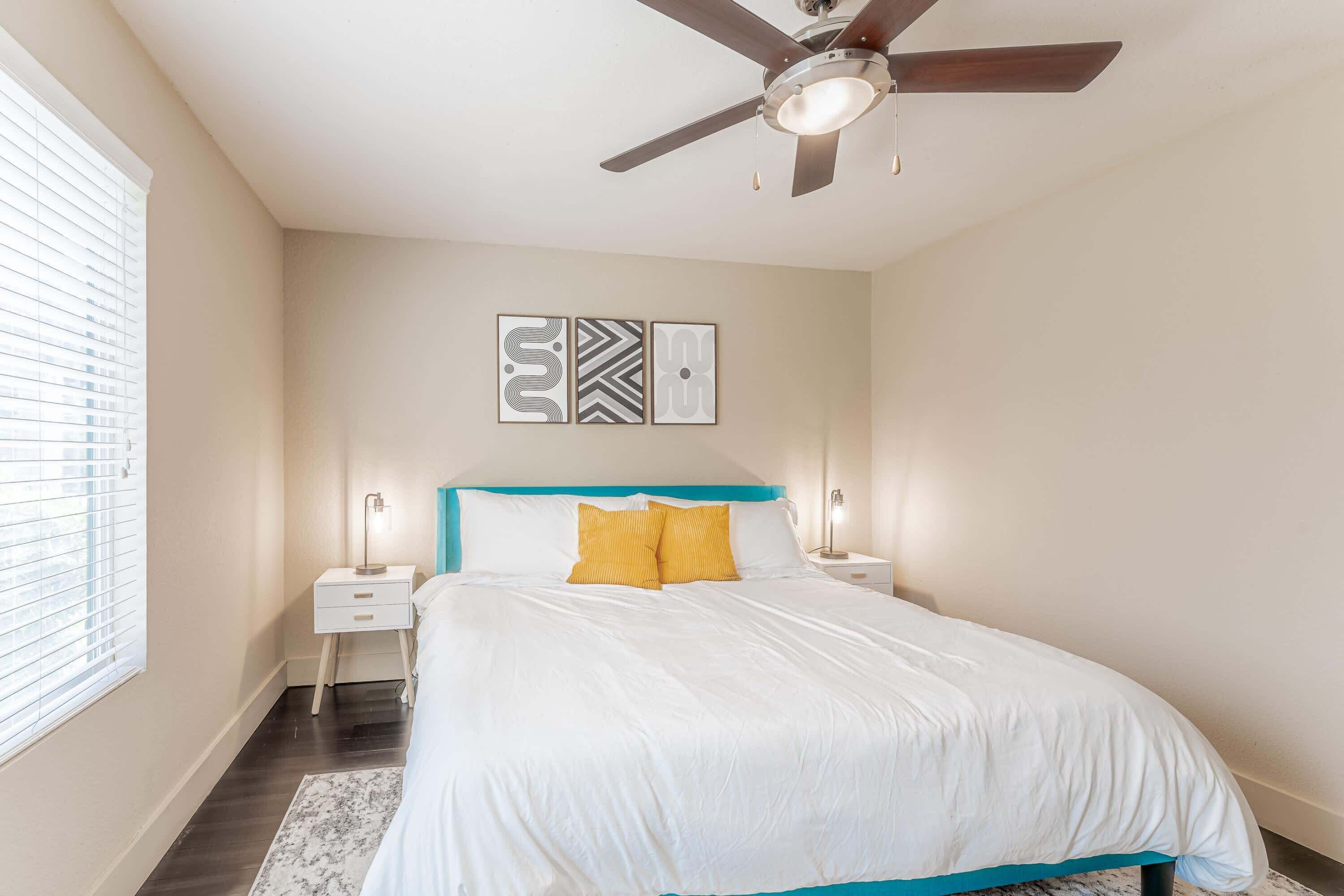 A bedroom with a bed, a ceiling fan, bedside tables, and wall art.
