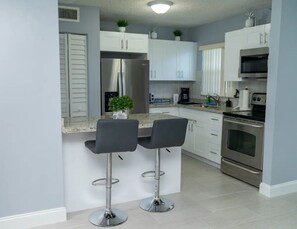 A modern kitchen with two bar stools, stainless steel appliances, and white cabinetry. - Beautiful condo mins from beach, airport & casinos (margate)