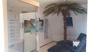 En moderne stue med en glasvæg, en stor palme og en mørkeblå sofa.