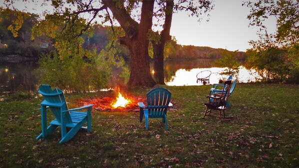 Eine Seenlandschaft mit drei Adirondack-Stühlen, die um ein Lagerfeuer platziert sind.