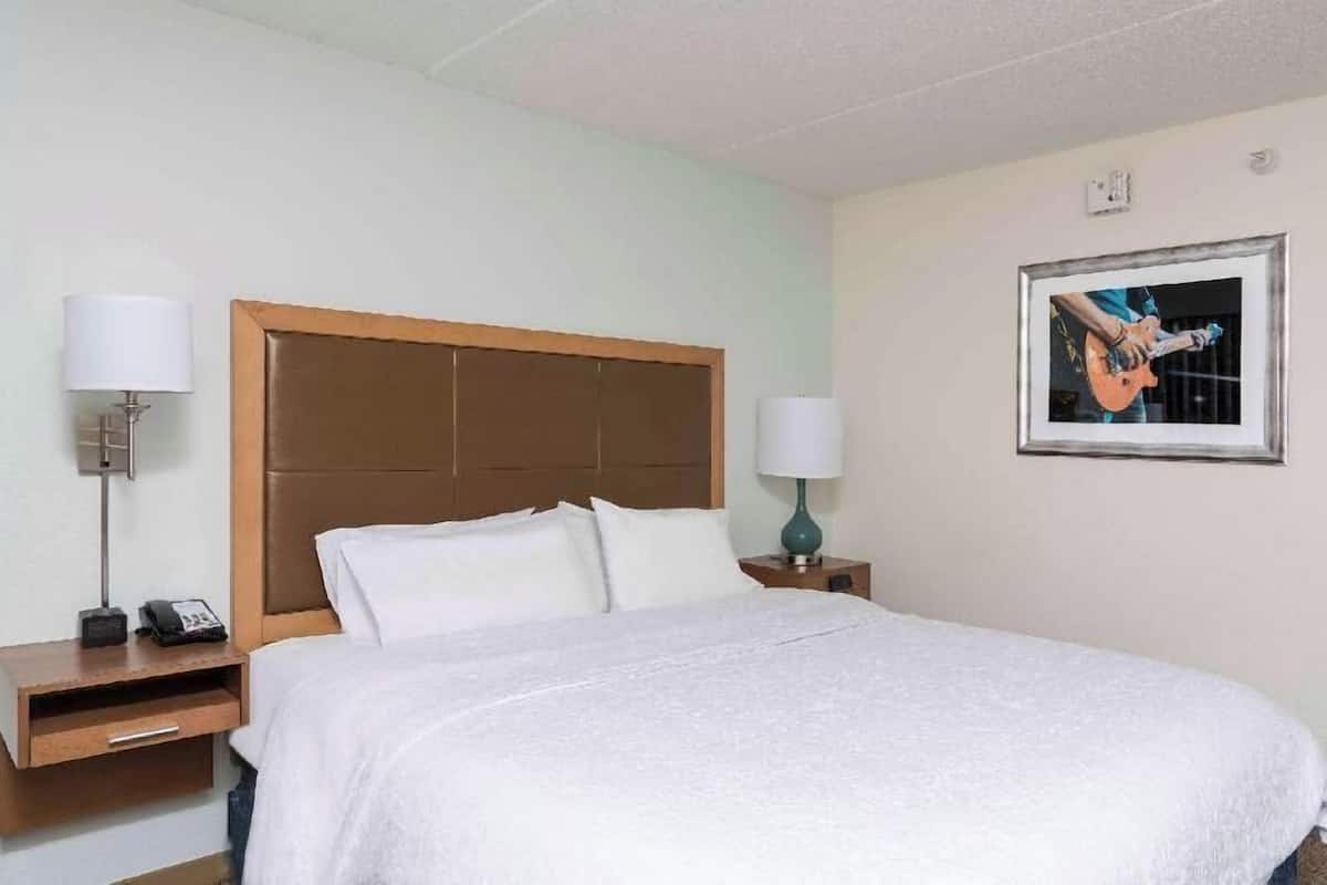 A hotel room with a bed, two bedside lamps, a nightstand with a phone, and a framed picture on the wall.