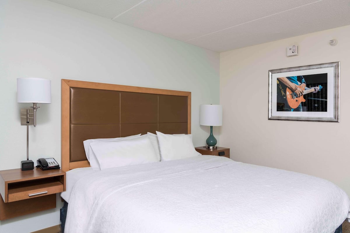 A hotel room with a bed, two bedside tables, a lamp, a phone, and a framed picture on the wall.
