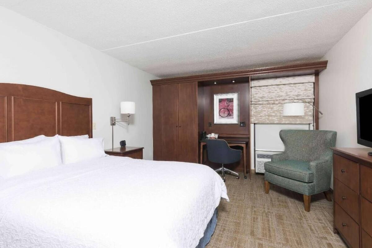 A hotel room with a large bed, a desk with a chair, a television, and a wardrobe.