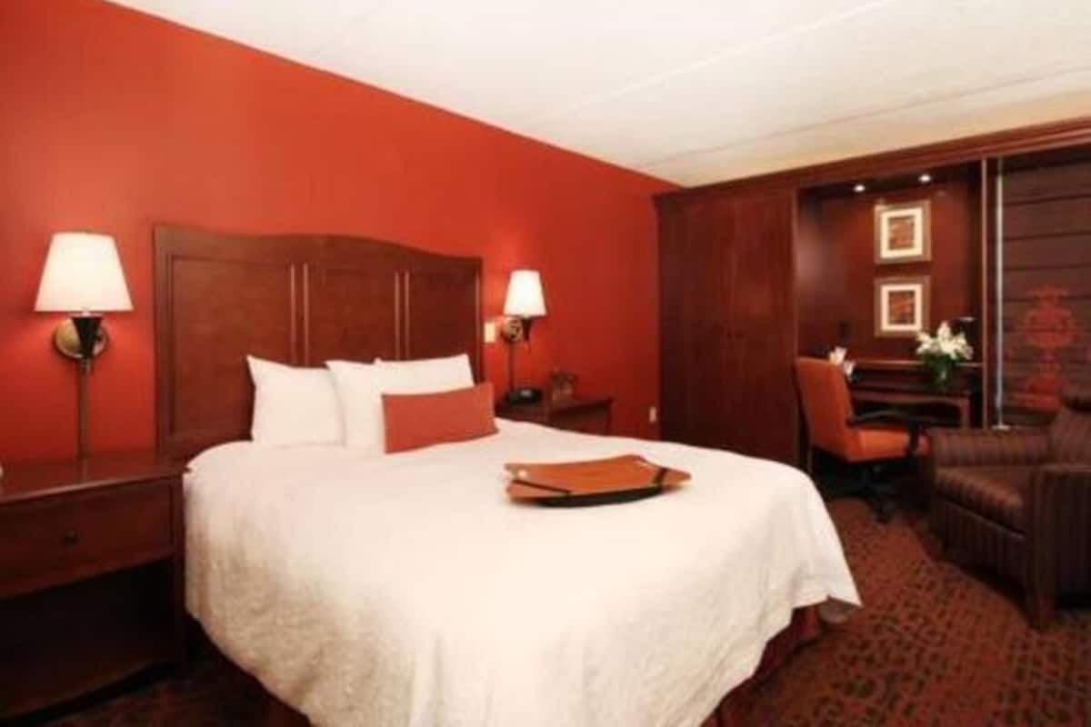A hotel room with a large bed, two bedside tables, a chair, and a desk with a lamp.