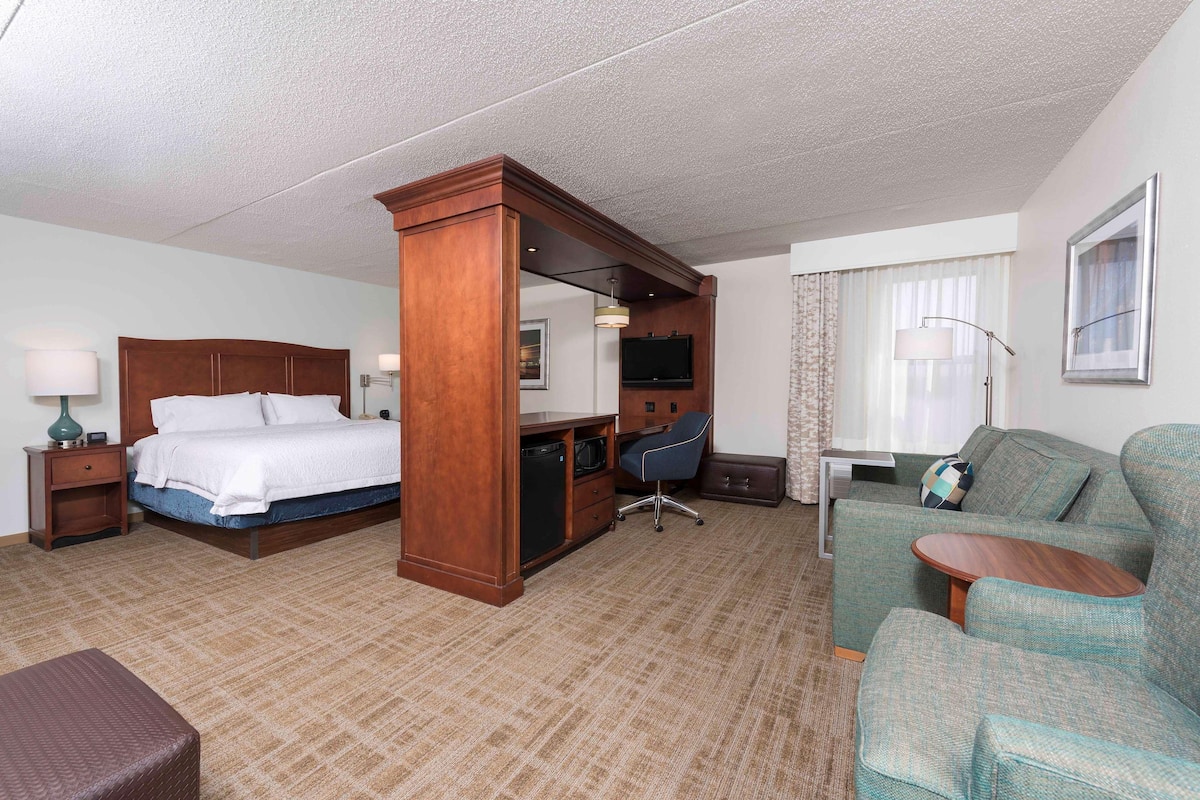 A hotel room with a bed, desk, chair, sofa, and a small table.