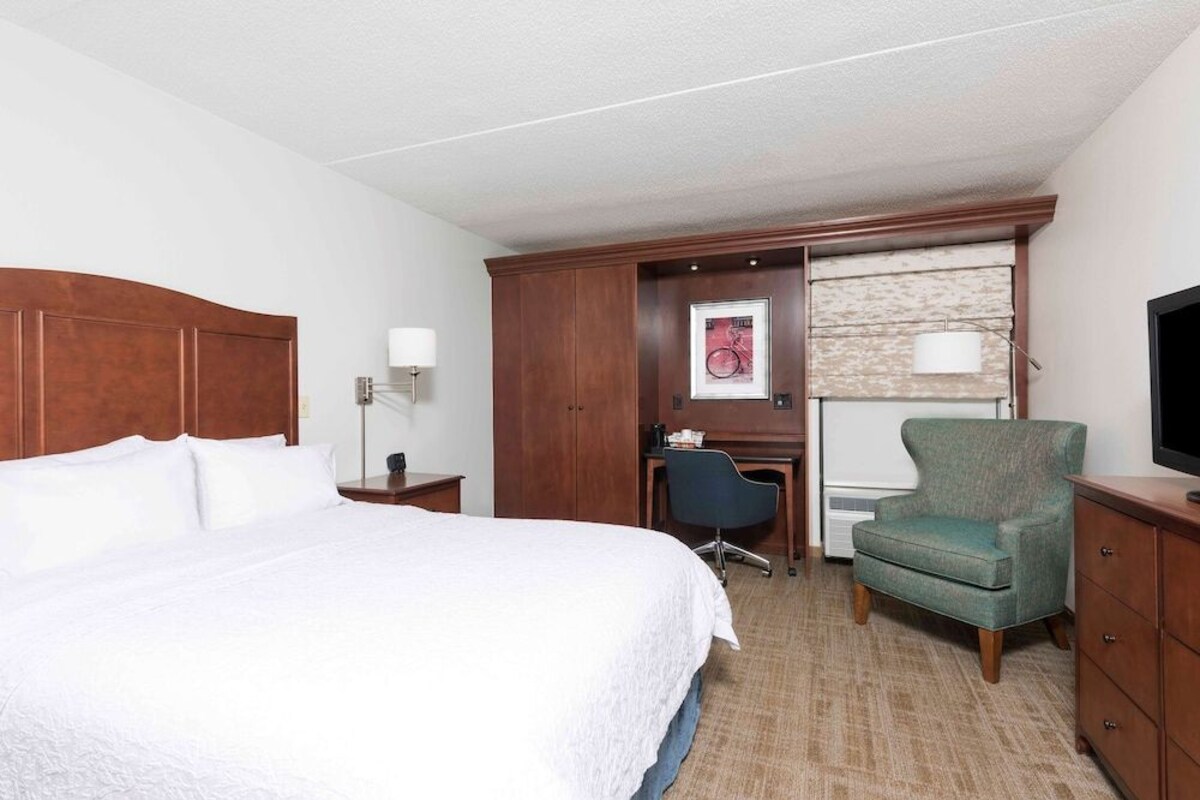 A hotel room with a large bed, a desk, a chair, a television, and a wardrobe.