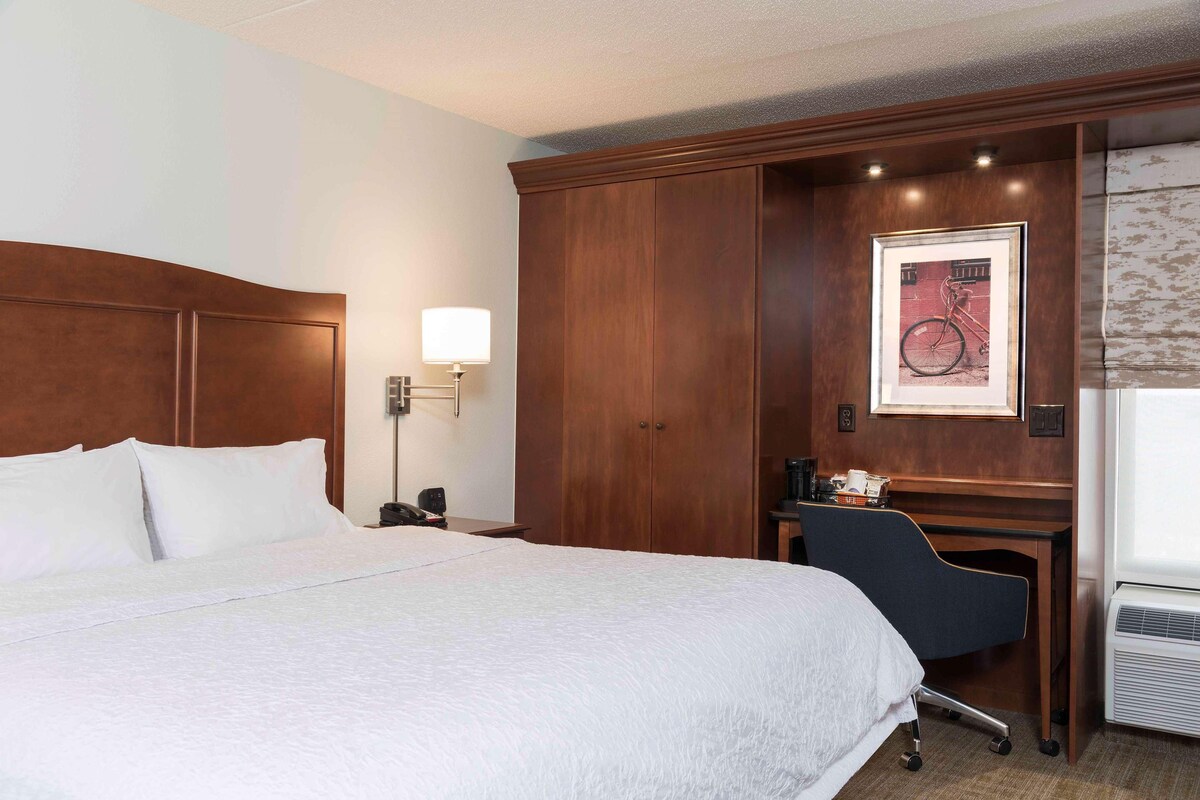 Une chambre d’hôtel avec un grand lit, un bureau, une chaise, une lampe et un tableau encadré au mur.