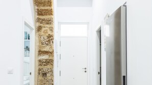 A narrow hallway with a stone wall, a white door, and a stainless steel refrigerator. - El Arco del Fotografo by Cadiz Time (Cádiz)