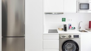 A compact kitchen with a stainless steel refrigerator, a microwave, a washing machine, and a sink with a faucet. - El Arco del Fotografo by Cadiz Time (Cádiz)