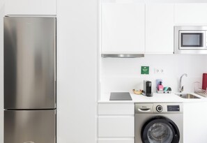 Une cuisine compacte équipée d’un réfrigérateur en acier inoxydable, d’un four à micro-ondes encastré, d’un lave-linge et d’un évier avec un robinet.