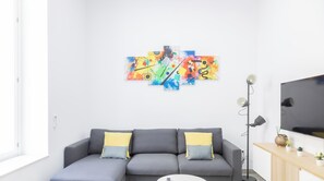 A modern living room with a grey sectional sofa, a flat-screen TV, a floor lamp, and a colorful abstract painting on the wall. - El Arco del Fotografo by Cadiz Time (Cádiz)