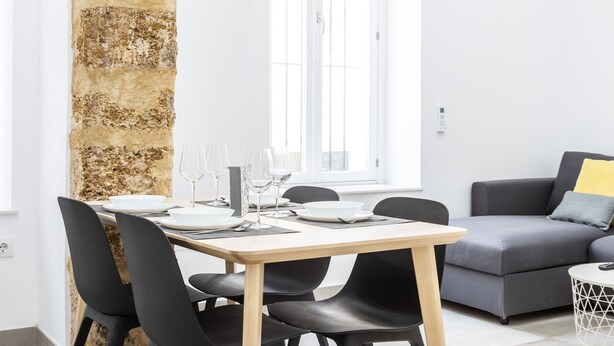A dining area with a stone column, a table set for four, and a grey sofa with a yellow pillow. - El Arco del Fotografo by Cadiz Time (Cádiz)