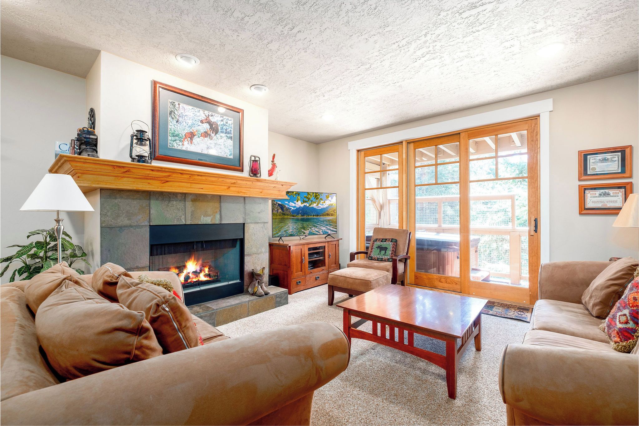 Living room with stone fireplace, TV, comfortable seating and large windows with natural light.