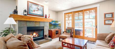 Living room with stone fireplace, TV, comfortable seating and large windows with natural light.
