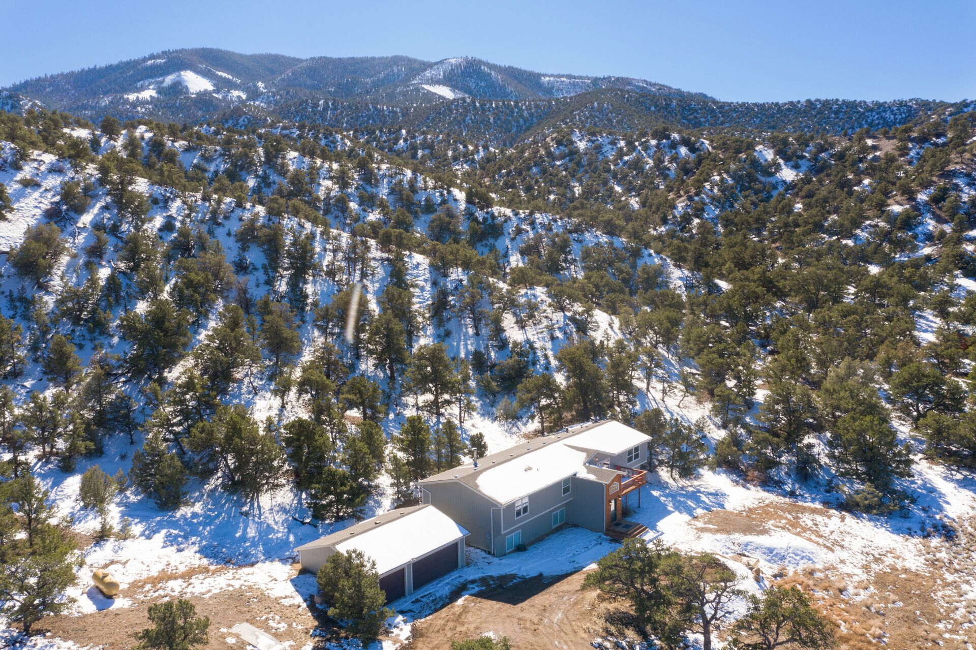 Un bâtiment doté d’un toit plat, entouré d’un paysage enneigé et de pins, avec des montagnes en arrière-plan.