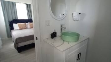Una habitación de hotel con una cama, un baño con un lavabo verde, un espejo y una alfombra a rayas.