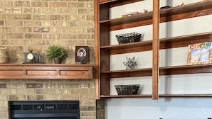 A living room with a brick fireplace, wooden shelves, a brown sofa, and a glass coffee table.