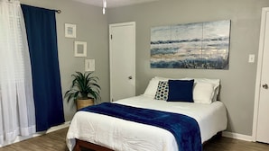 A bedroom with a bed, a potted plant, and a painting on the wall.