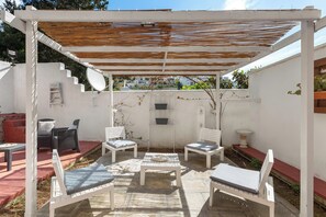 A covered patio area with white furniture, a table, and a pergola with a wooden roof.