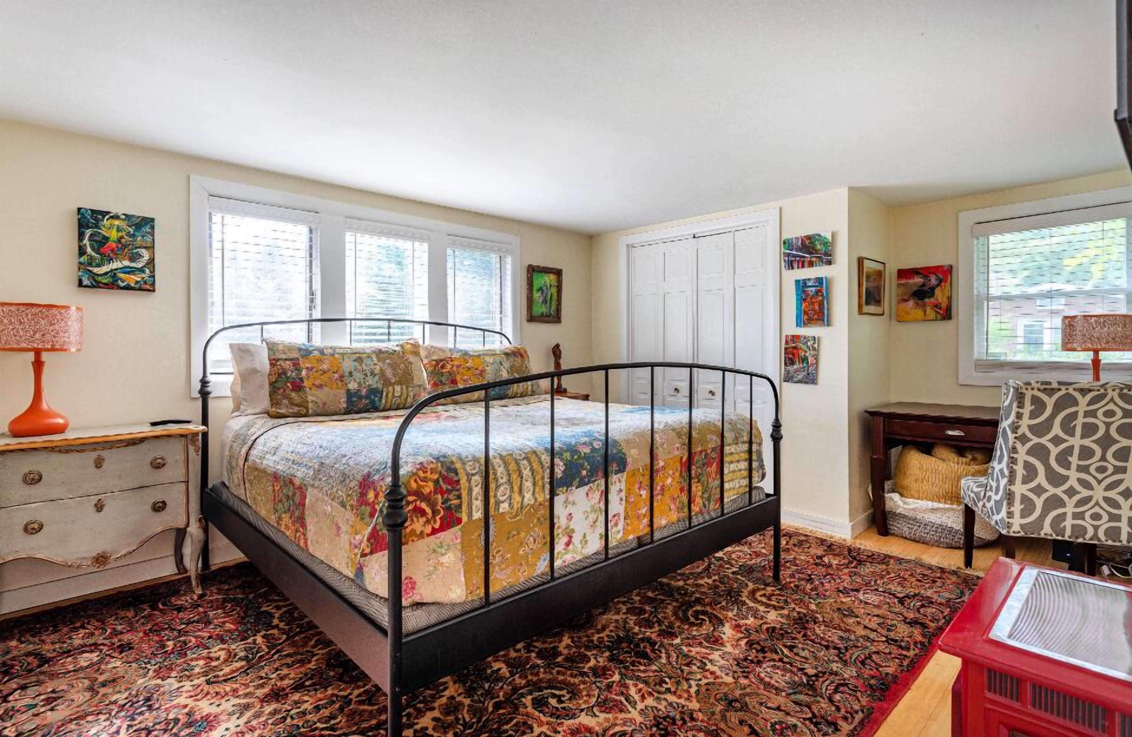 A bedroom with a metal bed frame, a patterned rug, a dresser, and a chair.