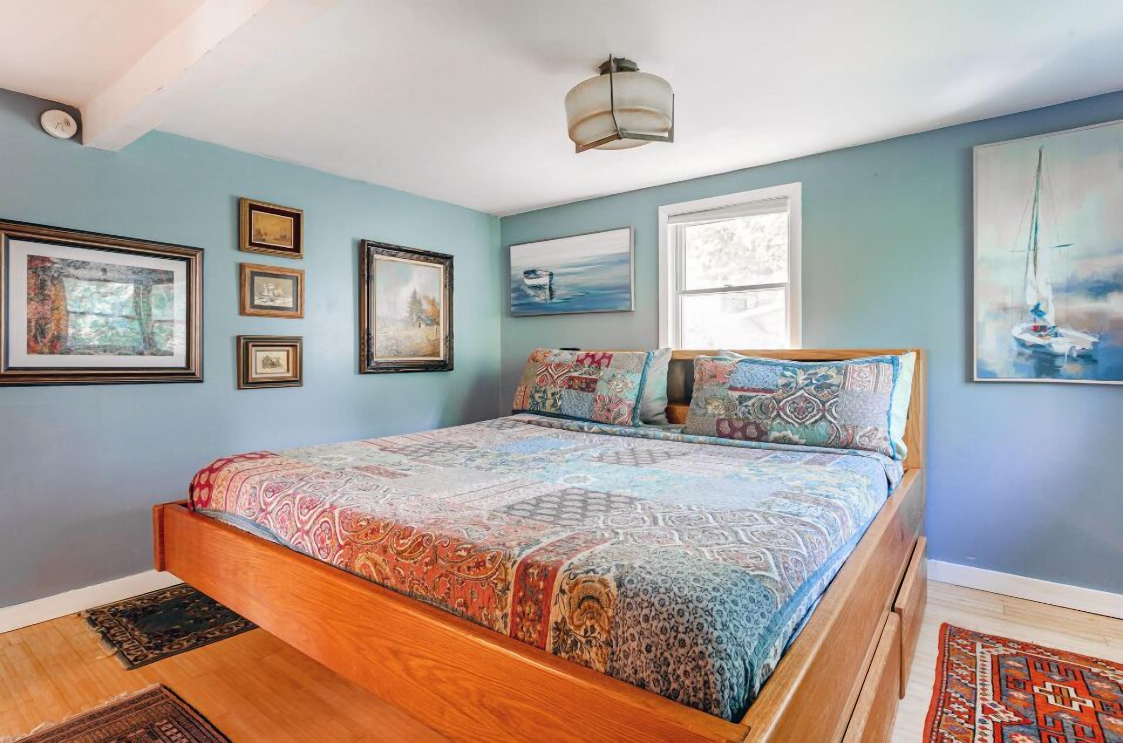 A bedroom with a wooden bed, multiple framed artworks on the wall, and a large window.